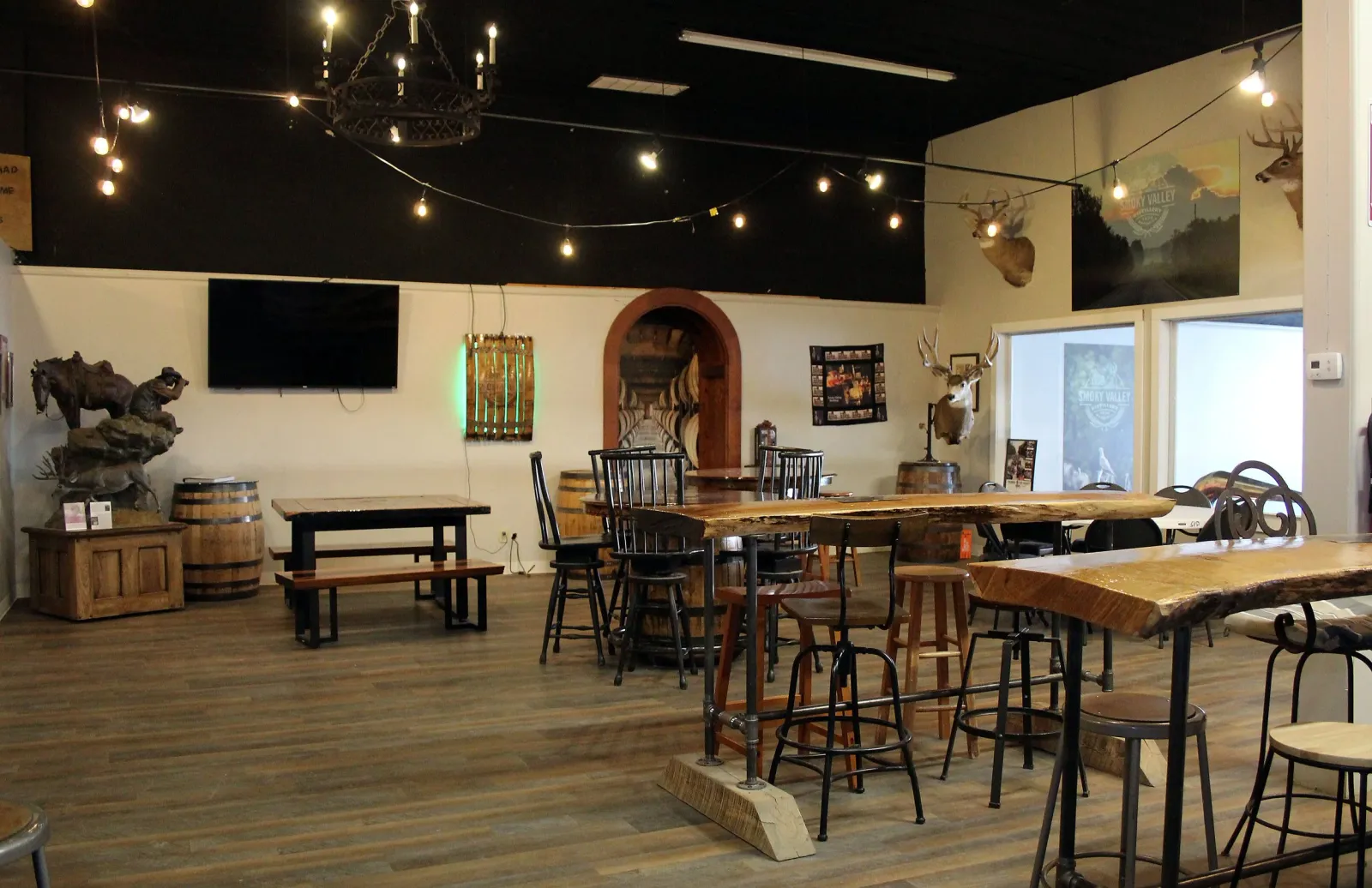 The venue room at Smoky Valley Distillery under string lights with high-top tables and barrels